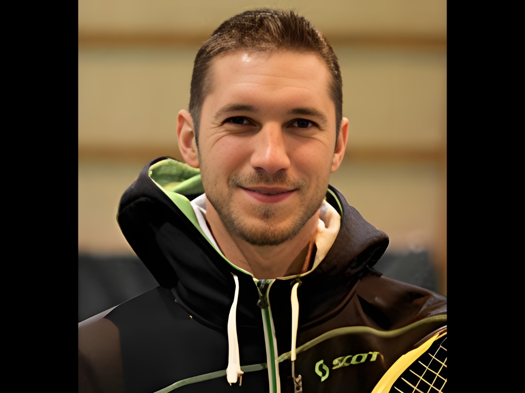 man in orange shirt and black shorts holding black and white tennis racket